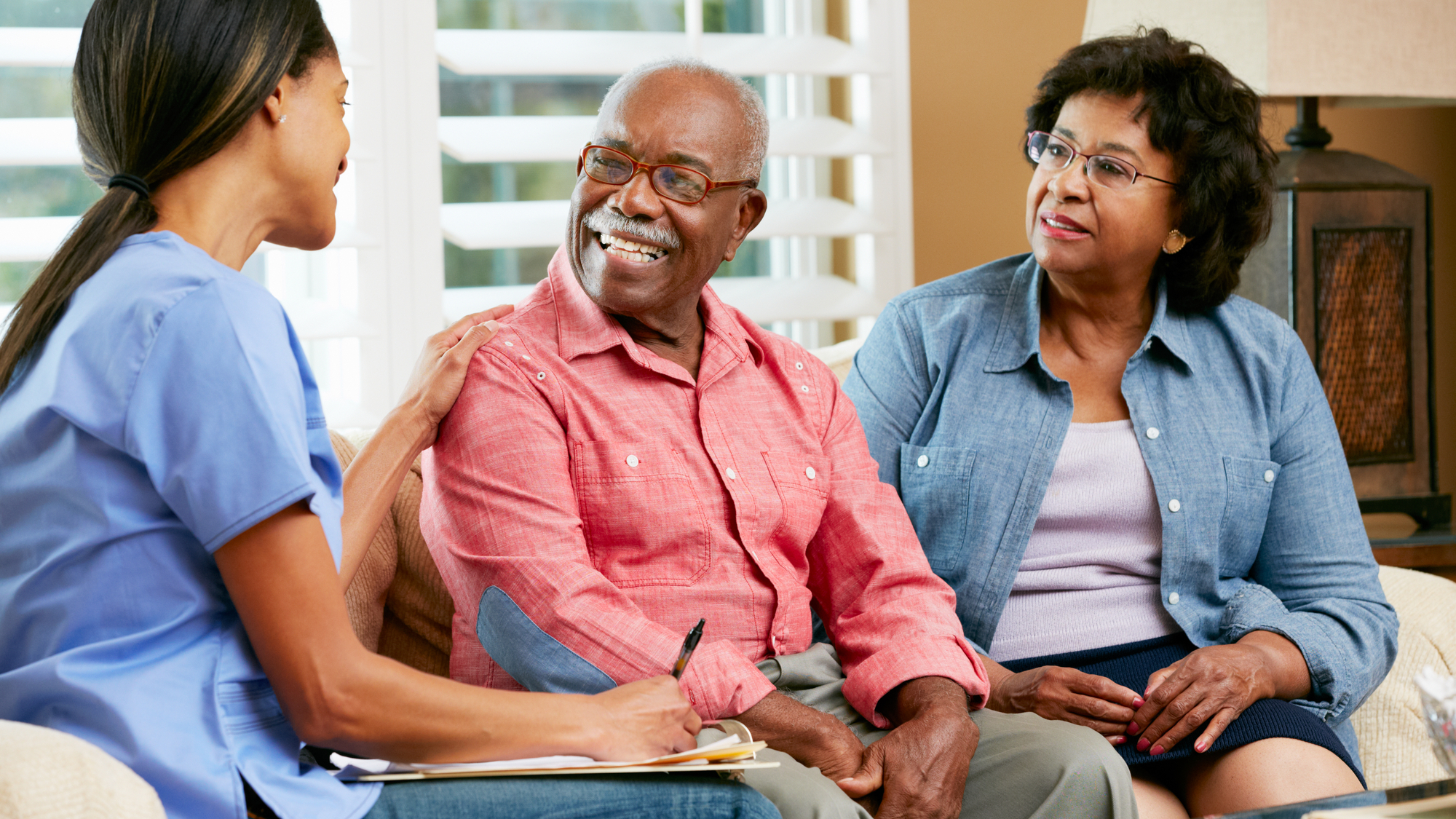 Nurse Making Notes During Home Visit With Senior Couple